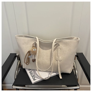 Détail d'un grand sac cabas blanc crème en similicuir avec un pendentif en peluche marron