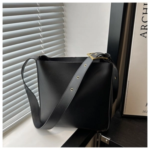Detail of minimalist black bucket bag featuring golden buckle and wide shoulder strap