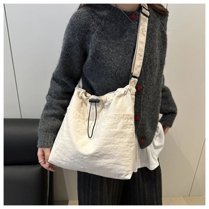 Detail of cream nylon tote bag showing drawstring closure and adjustable strap on model