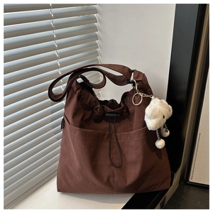 Detail of dark brown tote bag with drawstring texture and plush bear charm on a window sill