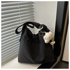 Detail of black drawstring tote bag with white cloud plush pendant and wide shoulder strap
