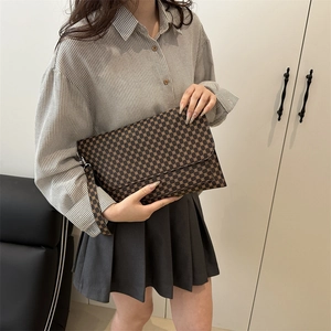 Brown geometric pattern clutch bag with wrist strap shown in a domestic setting