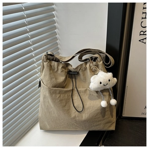 Detail of khaki nylon tote bag featuring drawstring closure and white cloud plush charm