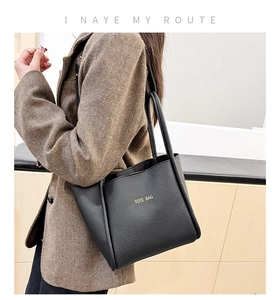 Close-up of black lychee grain leather tote bag with gold lettering on suit-clad model