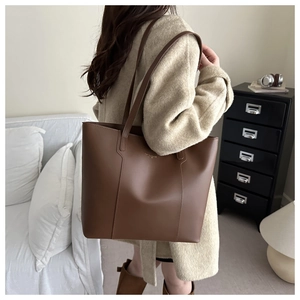 Close-up of brown faux leather tote bag with gold logo on a model in beige coat