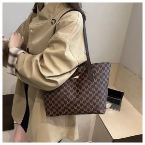 Close-up of retro brown tote bag with repeating M letter patterns and slim leather strap