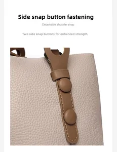 Detail of grey pebbled leather bag with brown strap attachment and secure snap buttons