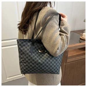 Detail of dark grey tote bag with M-pattern print and gold metal plaque on suit model