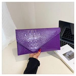 Detail view of purple crocodile texture envelope clutch held by a model in a casual setting