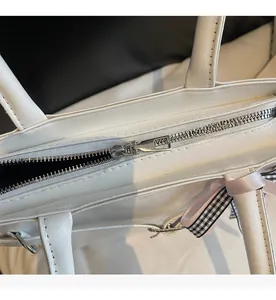 Détail du zip argenté et ruban à carreaux sur un sac à main blanc en similicuir