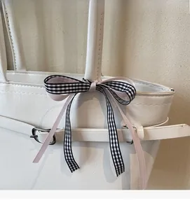 Détail du sac à main blanc en simili cuir avec boucle argentée et nœud en ruban à carreaux