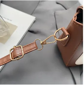 Detail view of the brown leather bag strap with golden metal hardware and buckle