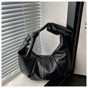 Detail of black pleated hobo bag featuring litchi grain texture and knotted wide strap