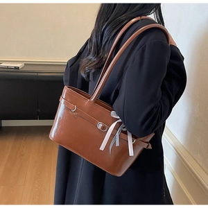 Borsa a spalla marrone lucida con fibbia metallica e fiocco a scacchi su modella
