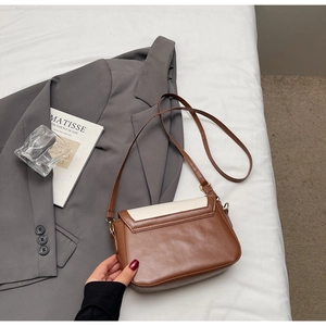 Detail of vintage brown and white leather crossbody bag on a modern gray blazer