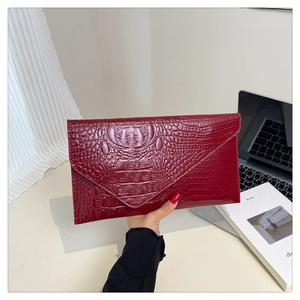 Detail of red crocodile embossed leather clutch bag held against a modern office background