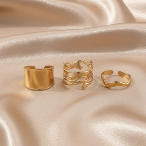 Detailed view of three gold-plated chunky rings on elegant champagne satin fabric