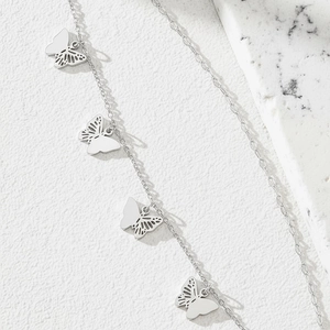 Minimalist silver butterfly pendant anklet with hollow design on marble background