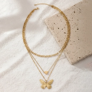 Three-layer gold stainless steel necklace with butterfly and heart charms on white sand