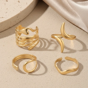 Detailed view of four irregular gold geometric rings on sand and silk backdrop