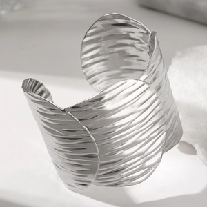 Macro detail of silver wide open bangle with organic wave texture on a stone background