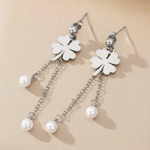 Silver four-leaf clover stud earrings with elegant pearl tassels on a textured surface