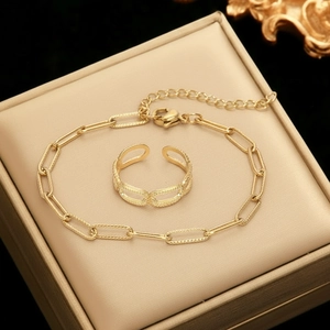 Detail of 18K gold-plated paperclip chain bracelet and matching ring on a beige display box