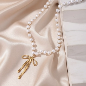 Elegante Perlenhalskette mit goldenem Schleifenanhänger auf luxuriösem Satinhintergrund