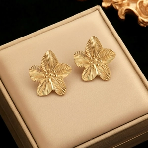 Detailed view of brushed gold flower earrings with petal textures in a beige jewelry box