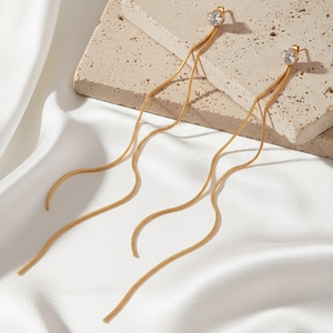 Detail of gold tassel earrings with zircon studs on stone and white silk fabric
