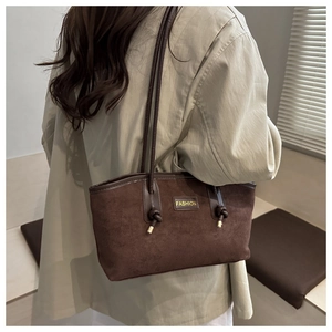Detail of dark brown suede tote bag with knotted shoulder straps and fashion logo tag