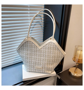 Detail of cream woven tote bag with V-shaped opening and gold metal logo plaque