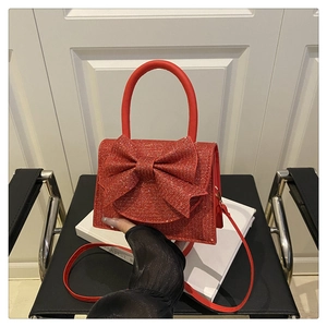 Close-up of red glitter evening handbag with large bow detail on a white book surface
