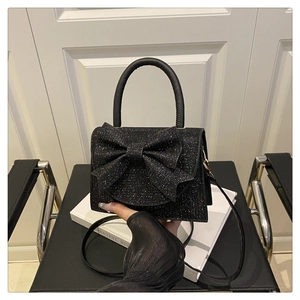Detail of elegant black glitter evening bag with a large bow and curved handle