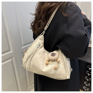 Detail of cream half-moon leather shoulder bag featuring a plush doll charm and long tassels