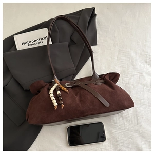 Detail of dark brown suede shoulder bag with beaded charm and smartphone for scale