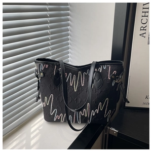 Detail of black tote bag with embossed letters, heart rhythm embroidery, and leather trim