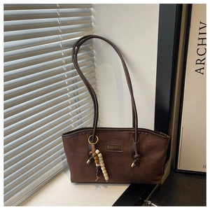 Detail of dark brown suede shoulder bag featuring a fashion patch and beaded pendant charm