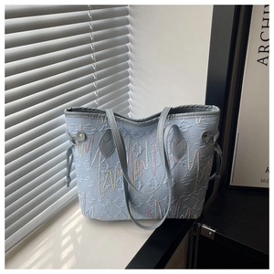 Close-up of light blue tote bag with colorful embroidery and letter embossed texture