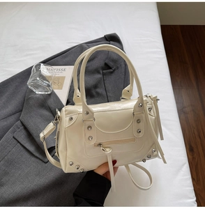 Dettaglio borsa in ecopelle bianco crema con borchie argentate e zip con nappe su un blazer