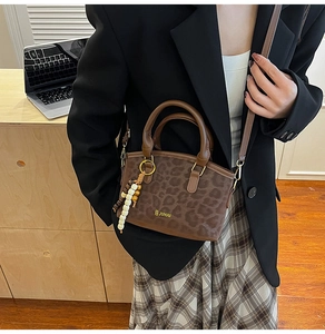 Detail of leopard print bucket bag featuring wooden bead tassel and metallic logo accent
