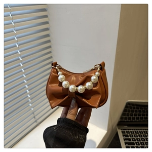 Detail of a brown bow-shaped mini handbag with pearl handle and golden hardware