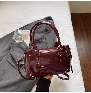 Dettaglio della borsa in pelle verniciata bordeaux con rivetti in metallo e cerniere stile moto