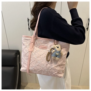 Detail of pink pleated tote bag with floral embroidery and teddy bear charm on shoulder