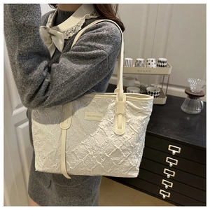 Dettaglio della trama floreale a rilievo e del logo sulla borsa tote bianca