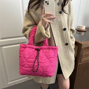 Pink quilted tote bag with heart embroidery and drawstring closure worn with a beige coat