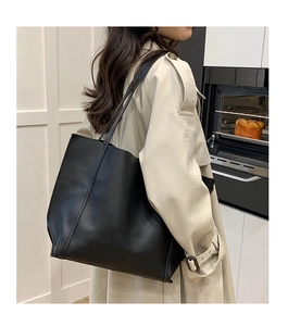 Close-up of a large black tote bag with long straps worn on shoulder in a kitchen