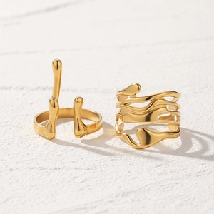 Detail of 18K gold plated minimalist liquid metal stackable rings on textured background