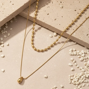 Close-up of double layer gold stainless steel necklace with waterdrop pendant on stone