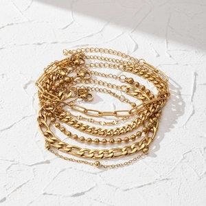 Golden stainless steel paperclip and bead chain 6-piece bracelet set on white textured surface